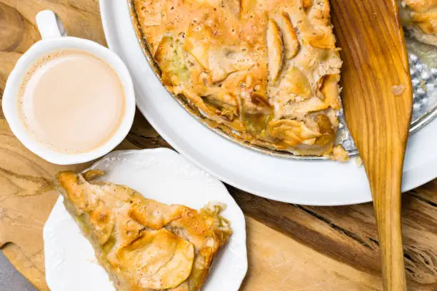 Photo of Apple crumble, Fresh baked pie and cup of coffee on the natural wood background on metal plate, closeup