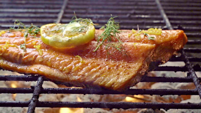 Wild Caught Salmon Filet on a Fiery Grill Topped with Lemon Slice and Herbs