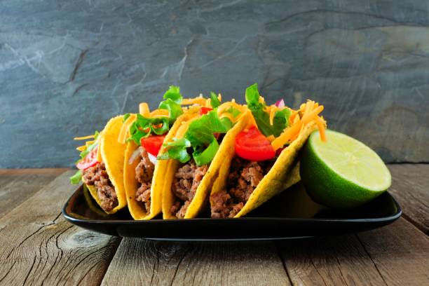 Hard shelled tacos on plate with a dark background Hard shelled tacos with ground beef, lettuce, tomatoes and cheese. Group on plate with a dark background. ground beef photos stock pictures, royalty-free photos & images