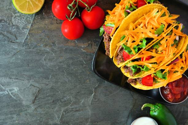 istock Hard shelled tacos with ground beef, vegetables and cheese, border on a dark background 1022490618