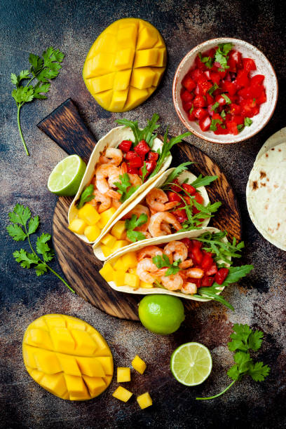 istock Mexican shrimp tacos with avocado, tomato, mango salsa on rustic stone table. Recipe for Cinco de Mayo party. Top view, overhead, flat lay. 1022515972