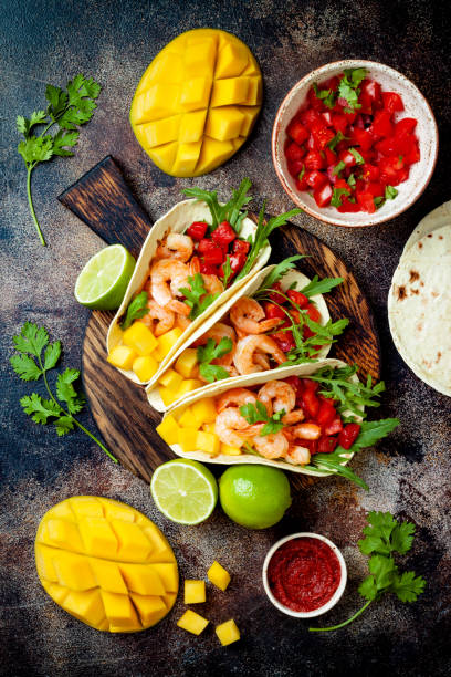 istock Mexican shrimp tacos with avocado, tomato, mango salsa on rustic stone table. Recipe for Cinco de Mayo party. Top view, overhead, flat lay. 1022515992