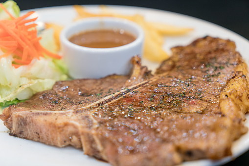 Tender grilled porterhouse or t-bone steak served with crisp golden French fries and fresh green herb salad accompanied by black pepper ketchup sauce.