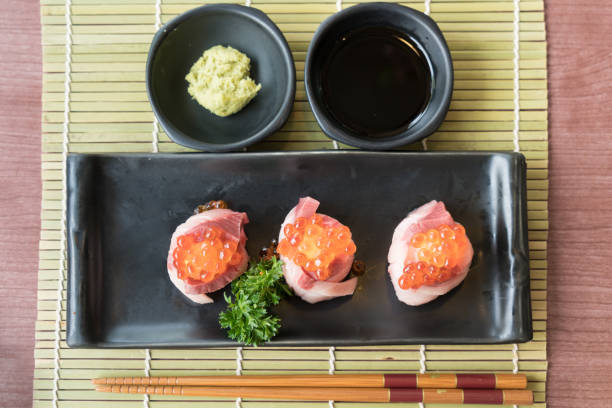 uova di salmone su sushi hamachi su piatto nero insieme a salsa giapponese e decorazione di foglie verdi, cibo giapponese, vista dall'alto al sushi. - sashimi white prepared fish hamachi foto e immagini stock