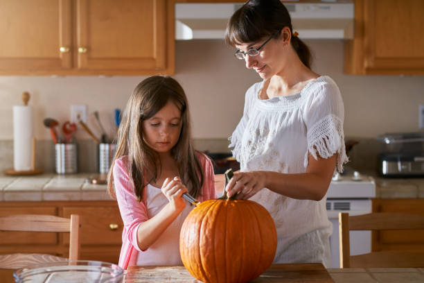 istock fun activity - mother and daughter having fun carving pumpkin 1022541634