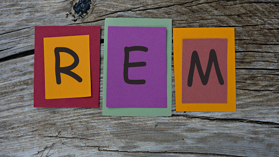 REM word written on colorful sticky notes on wooden background.