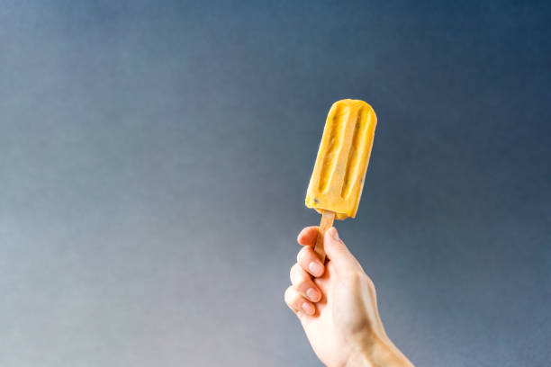 istock Hand holding juicy mango ice cream on a grey background. 1022727976