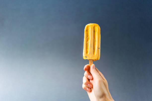 istock Hand holding bright yellow ice cream on a grey background. 1022729332