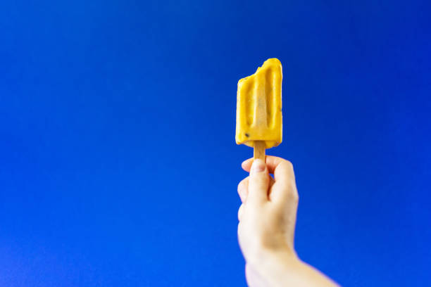 istock Hand holding bright yellow ice cream on a deep blue background. 1022730874