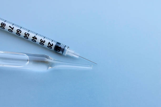 contenitore di fiale trasparente con medicina liquida vicino a una piccola siringa di insulina su sfondo blu. - antitoxin foto e immagini stock