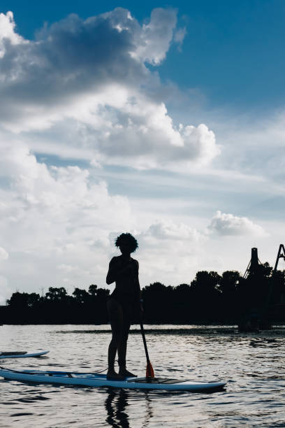 istock silhouette of sportswoman standing on paddle board on river with cloudy sky 1022745406