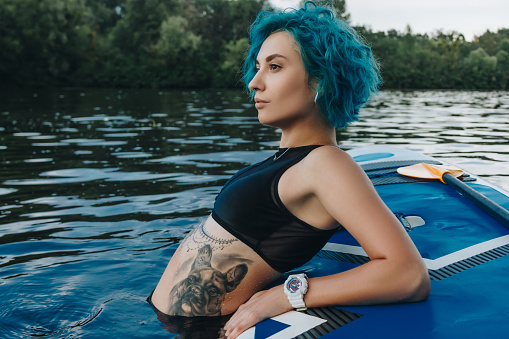 athletic young woman with blue hair relaxing on paddleboard in water