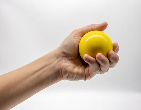 Hand holding yellow stress ball isolated on white background.