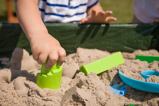 Toddler's hands playing with kinetic sand outdoors. Child making shapes.  Lifestyle and summer concept.