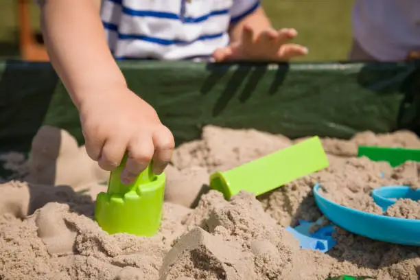 Toddler's hands playing with kinetic sand outdoors. Child making shapes.  Lifestyle and summer concept.