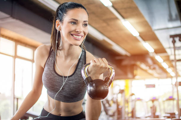 ritratto di bella ragazza sorridente con auricolari che sollevano pesi in palestra - picking up weight women sport foto e immagini stock