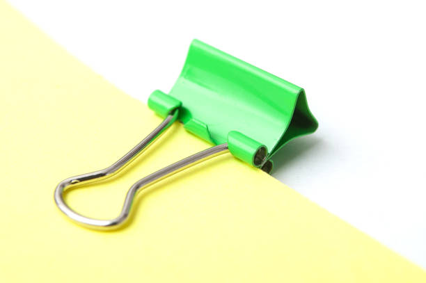 closeup of green paperclip on yellow paper on white background