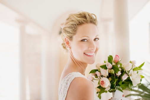 A radiant bride poses in an elegant strapless wedding gown, the train flowing behind her. Soft backlight from the window envelopes in a warm glow, enhancing the romantic ambiance