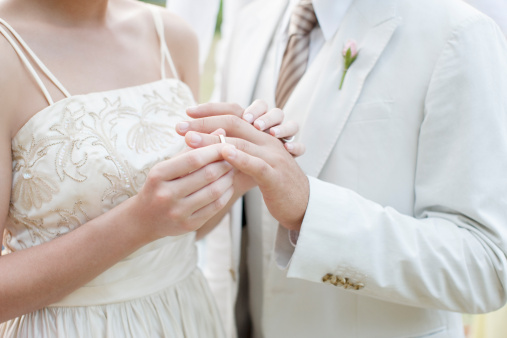 Closeup of young woman putting wedding ring on finger of husband during wedding ceremony, copy space