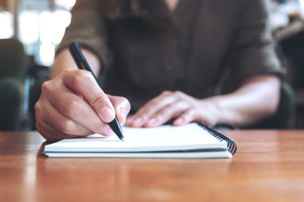 istock Closeup image of a woman writing down on a white blank notebook on wooden table 1022842496
