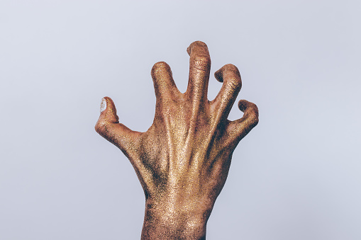 Creepy zombie hand close-up. Female palm with crooked fingers covered with golden glitter.