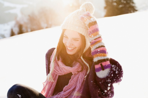 Happy young woman spinning in snowy winter park wearing warm knitted clothes and having fun outdoors. Girl enjoying winter. Seasonal activities