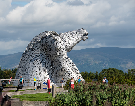 Falkirk, United Kingdom - August 09 2018:   Tourists around the Kelpies - a pair of large horse head statues made from Stainless steel by Sculptor Andy Scott and unveiled in 2013
