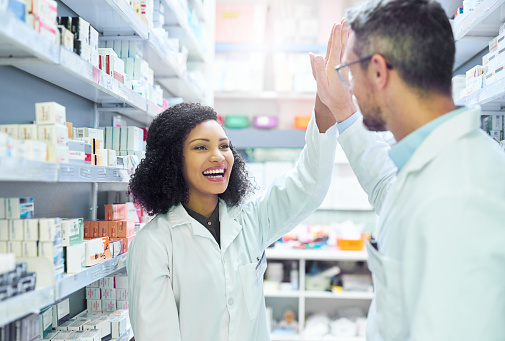 Shot of a mature man and young woman giving each other a high five while working in a pharmacy