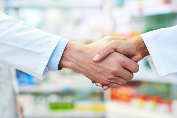 Partnered up to provide professional pharmaceutical care Cropped shot of two pharmacists shaking hands in a chemist mergers and acquisitions photos stock pictures, royalty-free photos & images