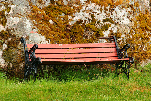Old wooden bench on green grass near the moss covered stone, Norway