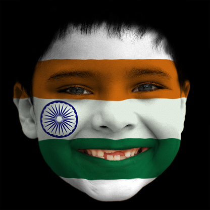 A lovely cheerful six year old boy smiling with broken incisors and half grown incisor teeth with Indian Tri Colour flag painted on his face. Saffron, White and Green stripes with Blue Ashoka Chakra