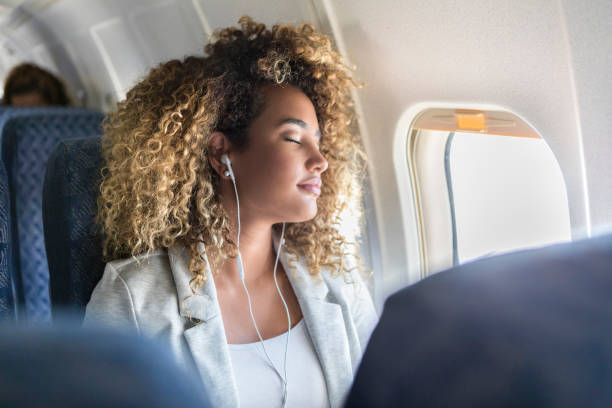 Young woman napping during flight Attractive young woman naps during long airplane flight. She is wearing earbuds. passenger cabin stock pictures, royalty-free photos & images