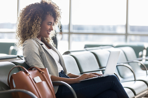 Young businesswoman waits for flight in airport terminal. She is using a laptop.
