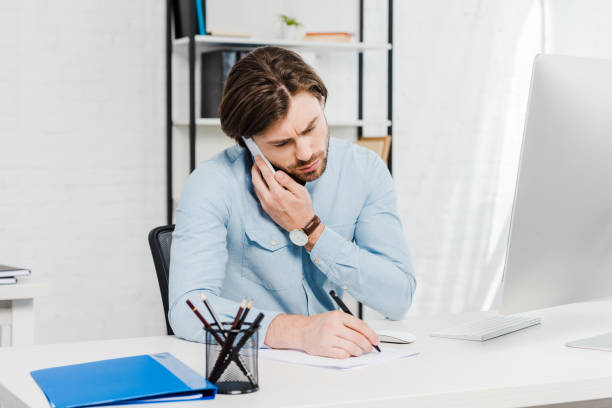 istock confident young businessman talking by phone and making notes at workplace 1022891812