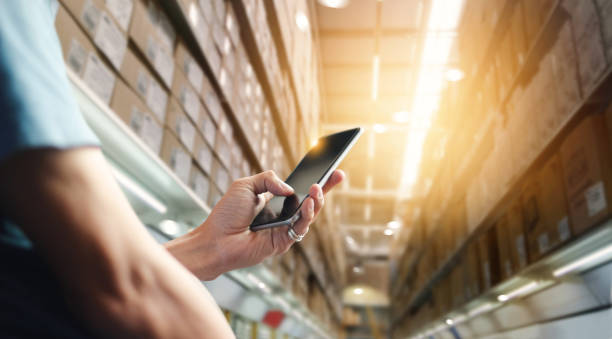 Factory worker using application on mobile smartphone to operate automation for modern trade. Checking order in large warehouse. Import and export the shipping cargo. Business marketing and technology