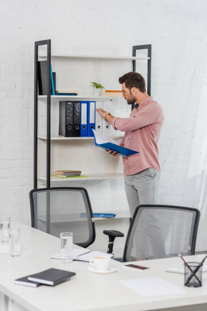 istock handsome young businessman taking folder from bookshelf at modern office 1022898814