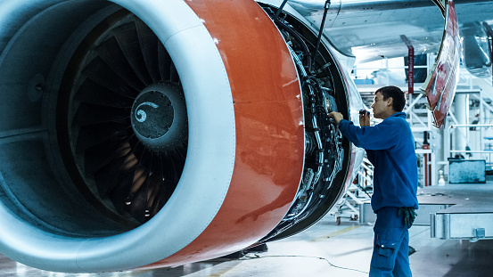 Mecánico de mantenimiento de aviones con una linterna inspecciona motor de avión en un hangar. photo