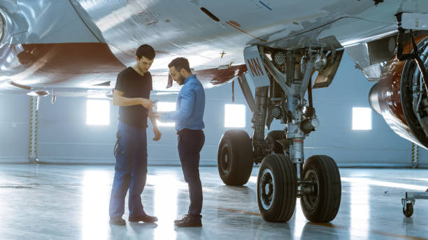 istock In a Hangar Aircraft Maintenance Engineer Shows  Technical Data on Tablet Computer to Airplane Technician. They Stand Near Clean Brand New Plane. 1022905238