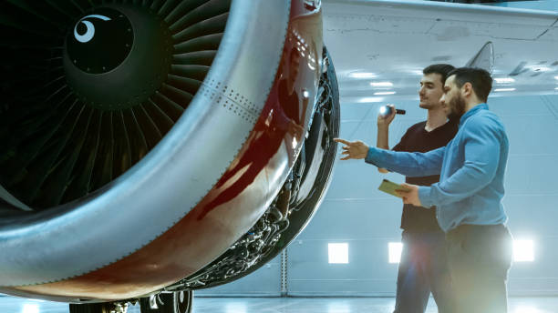 istock In a Hangar Aircraft Maintenance Engineer Shows Technical Data on Tablet Computer to Airplane Technician, They Diagnose Jet Engine Through Open Hatch. They Stand Near Clean Brand New Plane. 1022905260