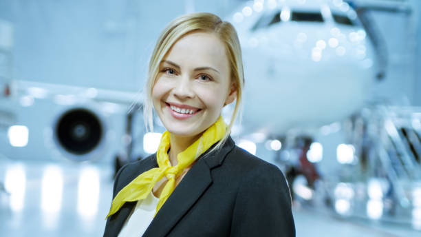 im flugzeug wartung hangar junge schöne blonde stewardess / flugbegleiter lächelt charmant vor der kamera. im hintergrund neue flugzeug ist sichtbar. - charmingly stock-fotos und bilder