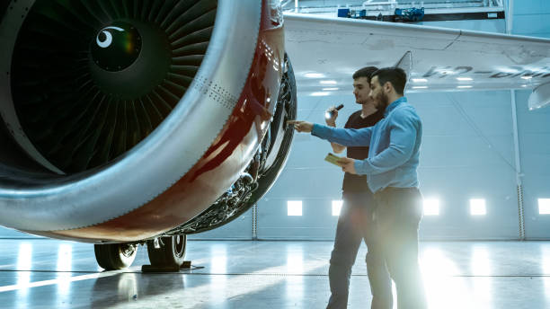 istock In a Hangar Aircraft Maintenance Engineer Shows Technical Data on Tablet Computer to Airplane Technician, They Diagnose Jet Engine Through Open Hatch. They Stand Near Clean Brand New Plane. 1022905278