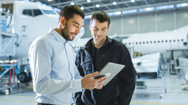 Aircraft Maintenance Worker and Engineer having Conversation. Holding Tablet. Aircraft Maintenance Worker and Engineer having Conversation. Holding Tablet. aerospace industry stock pictures, royalty-free photos & images