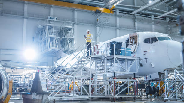 ingegnere in giubbotto di sicurezza in piedi accanto all'aereo in hangar - aerospace industry foto e immagini stock