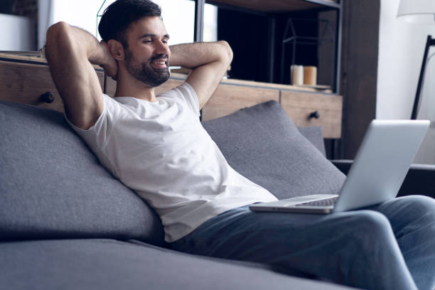 istock Typing new blog post. Side view of handsome young man using his laptop with smile while sitting on the couch at home. 1022917204
