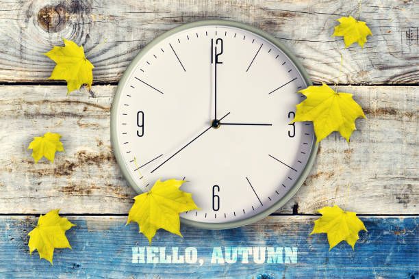 reloj y hermosas hojas de otoño amarillo sobre un fondo de madera. inscripción, hola otoño. - daylight savings fotografías e imágenes de stock