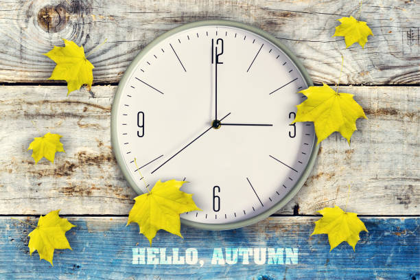 часы и красивые желтые осенние листья на деревянном фоне. надпись, здравствуйте, осень. - daylight savings стоковые фото и изображения