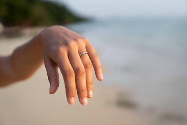 istock silver white engagement ring on fiancees hand - romantic proposal on beach 1022923972