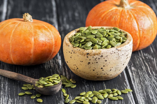 istock Bowl with raw pumpkin seeds on a rustic black table. Small orange pumpkins. selective focus 1022963182