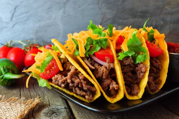 istock Hard shelled tacos with ground beef, vegetables and cheese, close up scene 1022990880