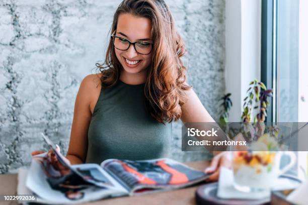 Photo libre de droit de Jeune Fille Avec Des Lunettes De Lecture Magazine À Proximité De La Fenêtre banque d'images et plus d'images libres de droit de Magazine